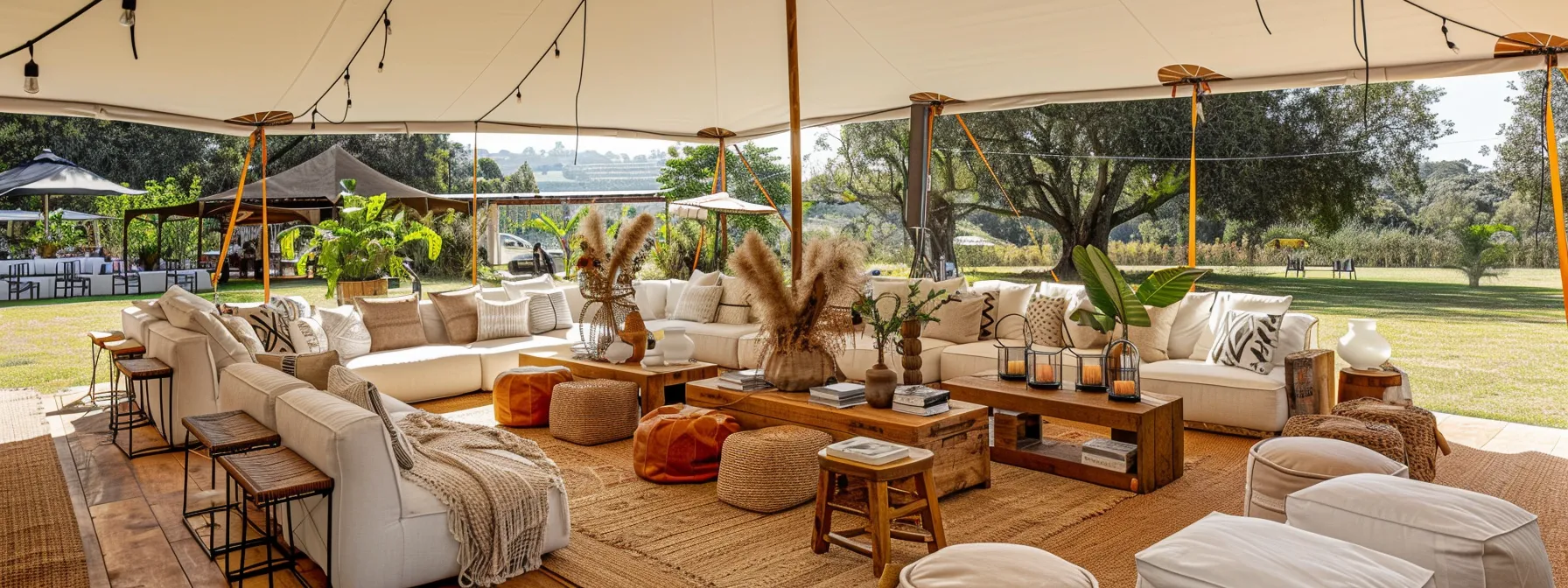 a vibrant outdoor event unfolds under a spacious open-air tent, showcasing an elegant arrangement of stylish furniture and decor that seamlessly blends with the surrounding natural scenery.